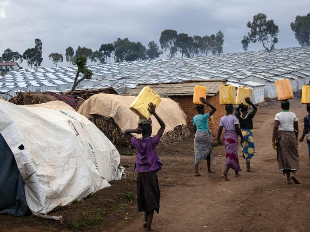 © UNHCR/Hélène Caux Des femmes retournent dans leurs abris sur le site de Plaine Savo pour personnes déplacées dans la province de l'Ituri après avoir récupéré de l'eau.